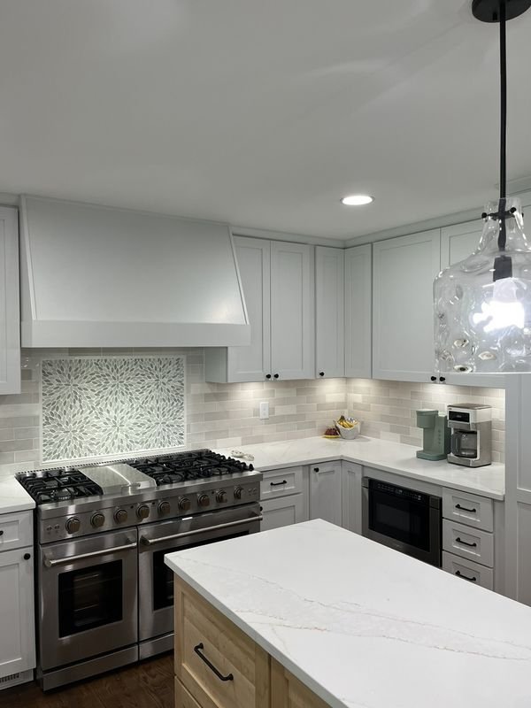 The same range wall after: a built hood over a range with a full-height tile backsplash and a light stone counter